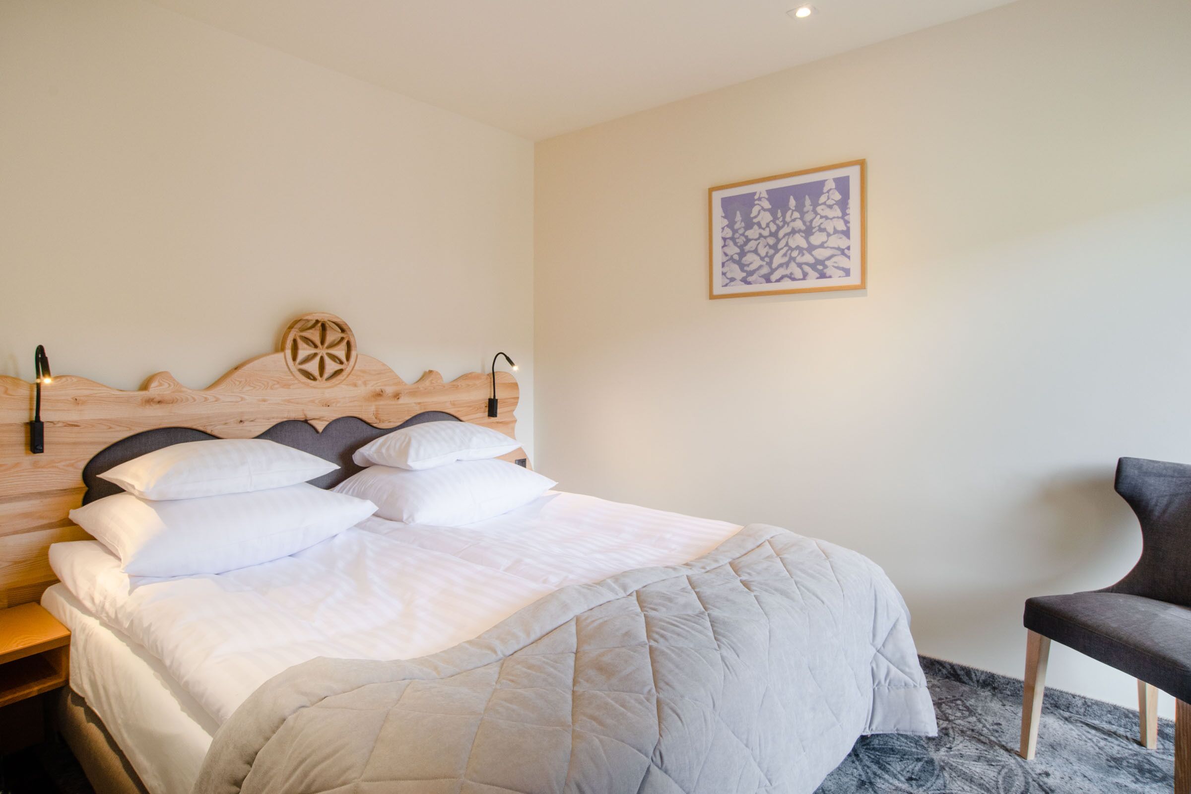 A neatly made bed with a quilted blanket, a wooden headboard with a decorative element, a bedside lamp, and a framed artwork on the wall.