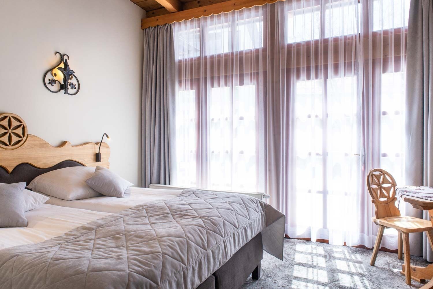 Un dormitorio con una cama grande, cabecera de madera, lámpara de pared y vista a través de cortinas traslúcidas.