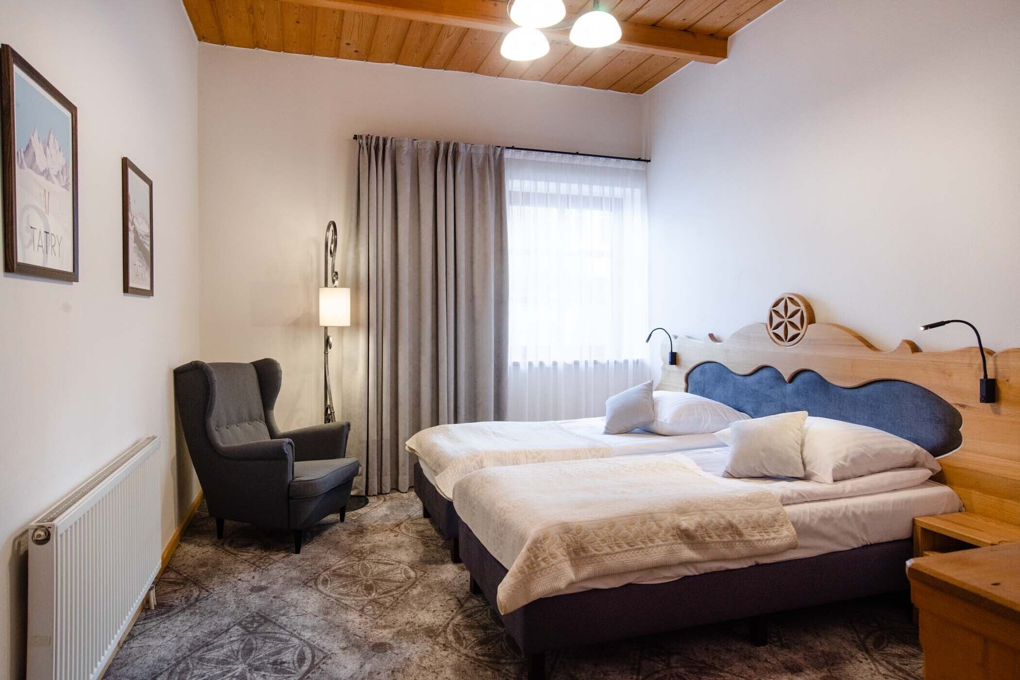 A bedroom with a bed, a chair, a bedside table, a lamp, and a window with curtains.