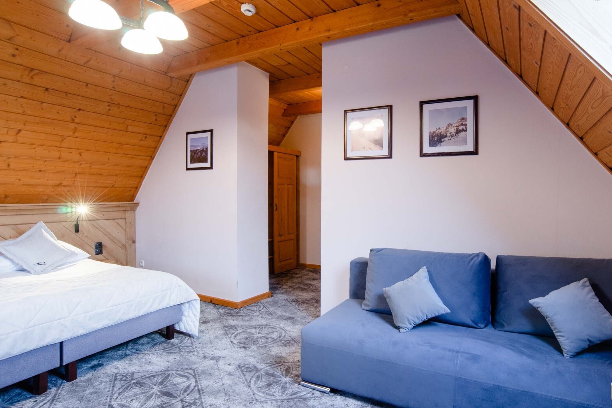 Quarto com uma cama, um sofá azul e duas imagens emolduradas na parede.