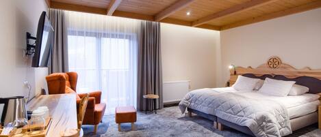 Habitación de hotel con techo de madera, cama con cabecera, escritorio con silla, una mesita y un televisor montado en la pared.