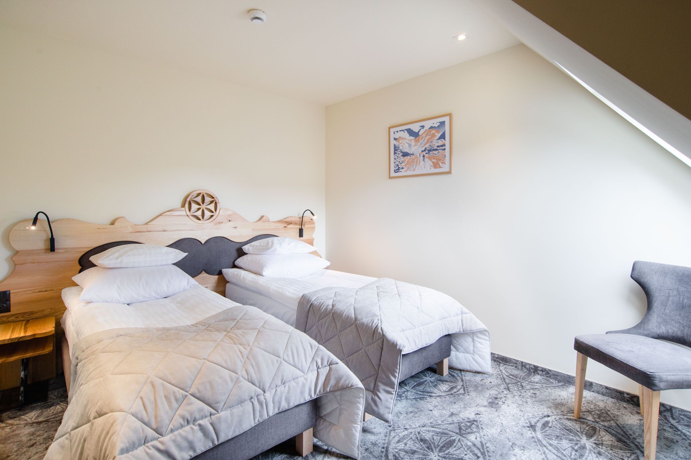 Une chambre d’hôtel avec deux lits, une chaise, une tête de lit en bois, une œuvre d’art accrochée au mur et un sol à motifs.