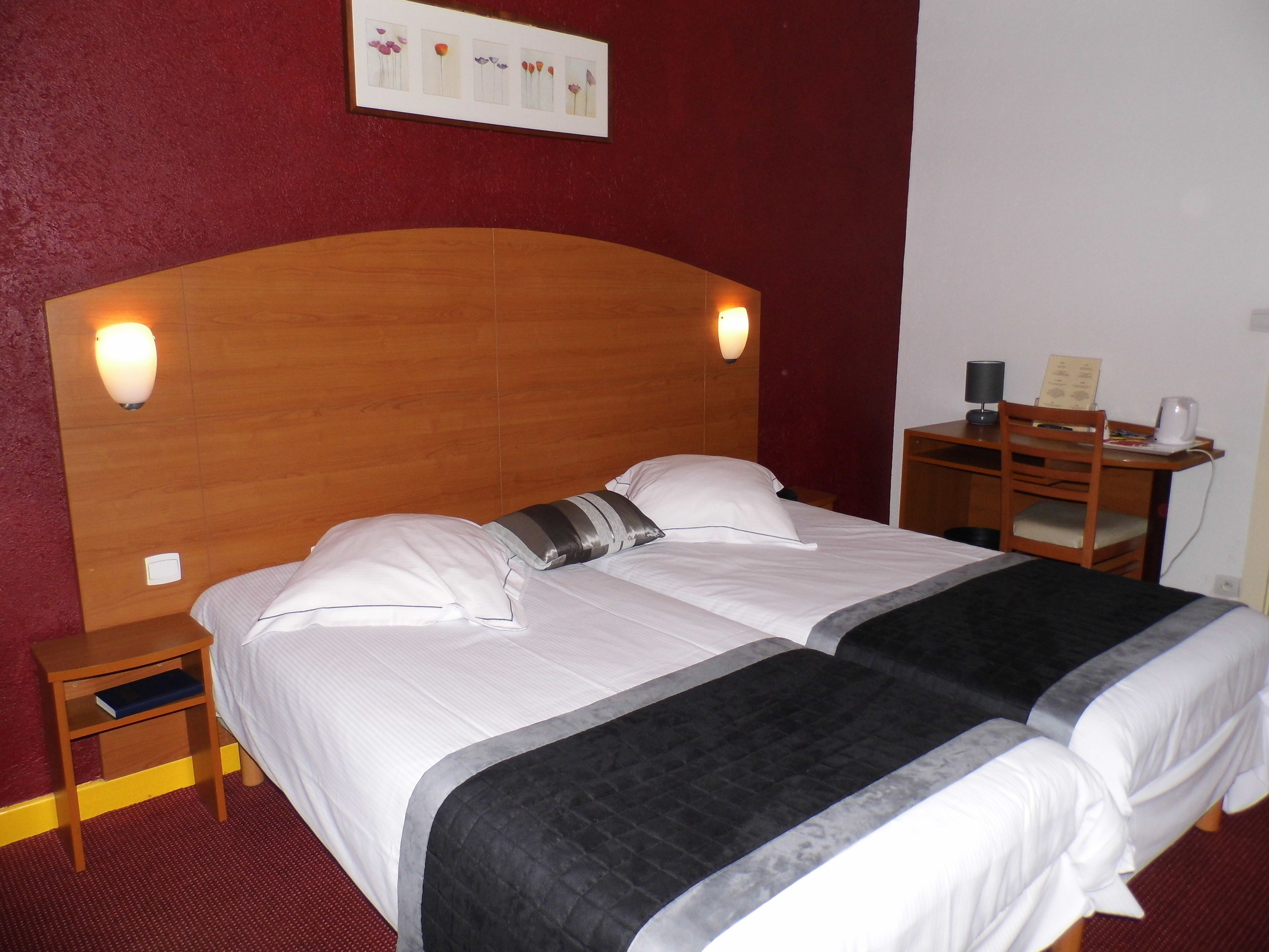 A double bed with a wooden headboard, two bedside tables, a desk with a chair, and a framed picture on the wall.