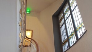 A curved staircase with a wooden handrail and a metal railing, leading to a room with a window featuring stained glass. - Hôtel Alerion (Metz)