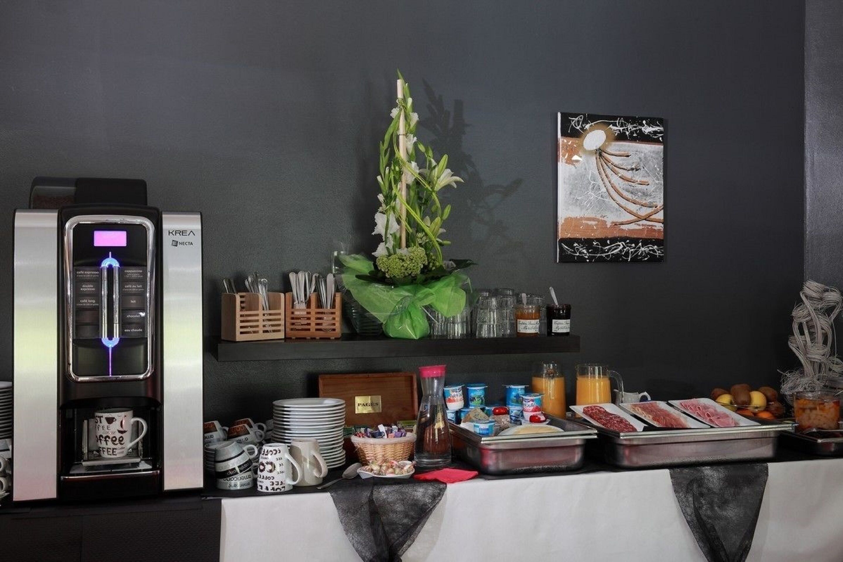 A breakfast buffet setup with a coffee machine, a variety of food items, and a decorative plant.