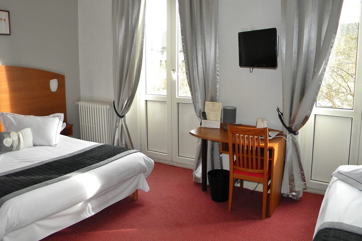 Ein Hotelzimmer mit Bett, Schreibtisch mit Stuhl, Fernseher und einem Fenster mit Vorhängen.