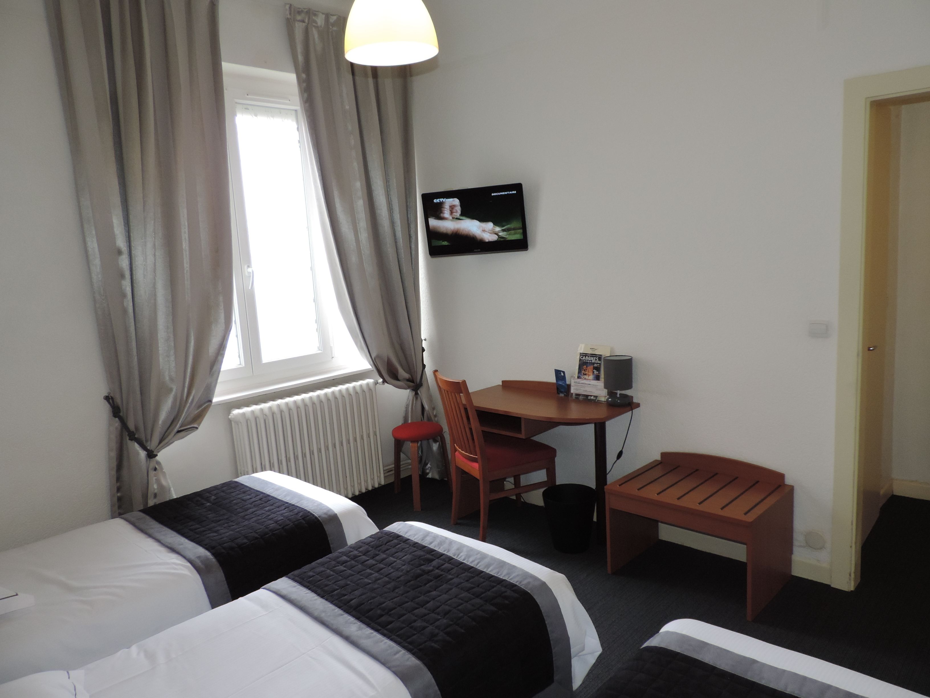 A hotel room with two beds, a desk, a chair, a television, and a window with curtains.
