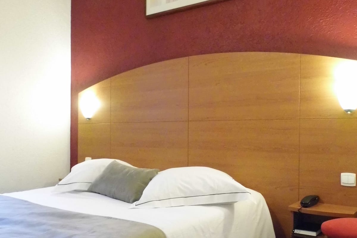 Ein Hotelzimmer mit einem großen Bett, einem Schreibtisch und einem Stuhl. Darüber hängt ein gerahmtes Bild an der Wand.