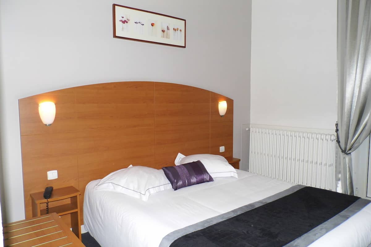 Ein ordentlich bezogenes Bett mit Holz-Kopfteil, zwei Nachttische mit Lampen, ein gerahmtes Bild an der Wand und eine Heizung.