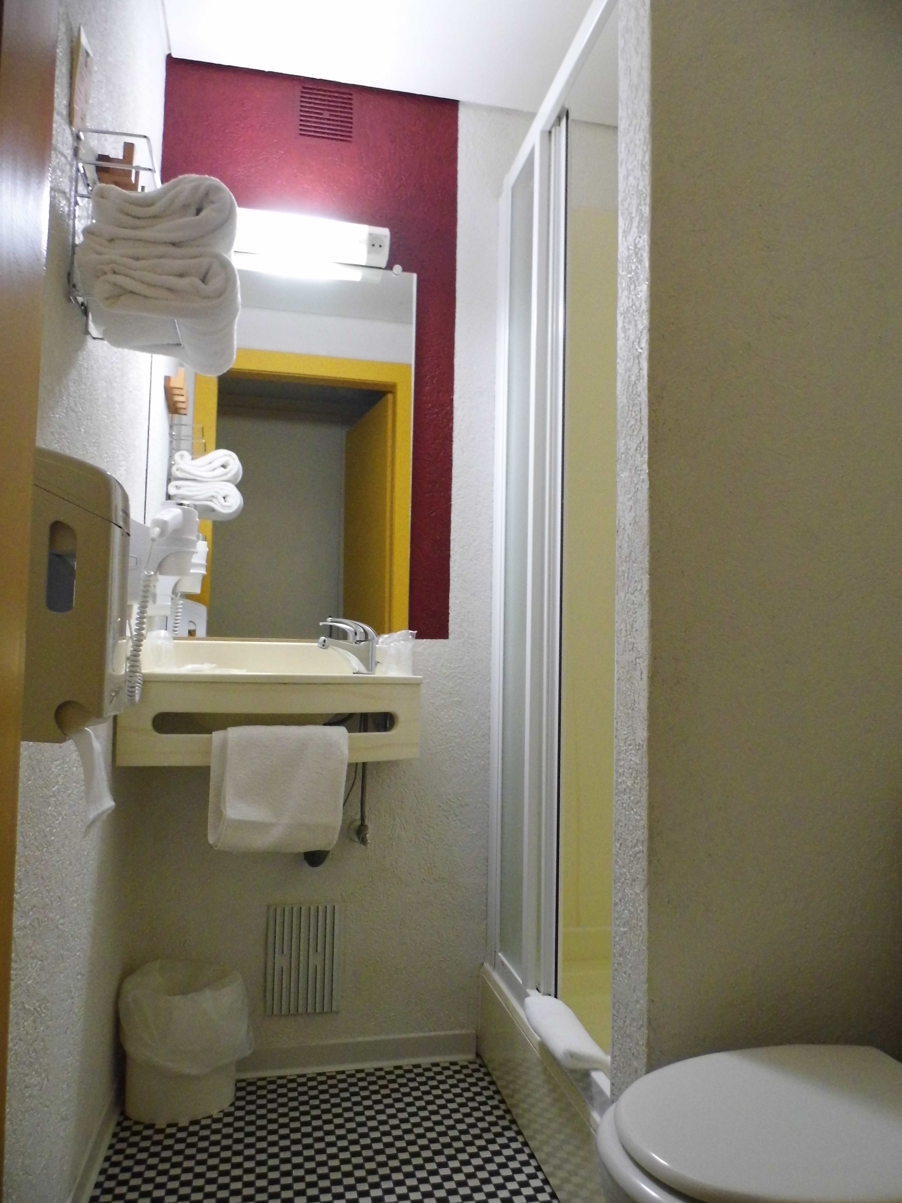 Un baño pequeño con piso de cuadros, un inodoro, un lavamanos con espejo y un perchero para toallas.