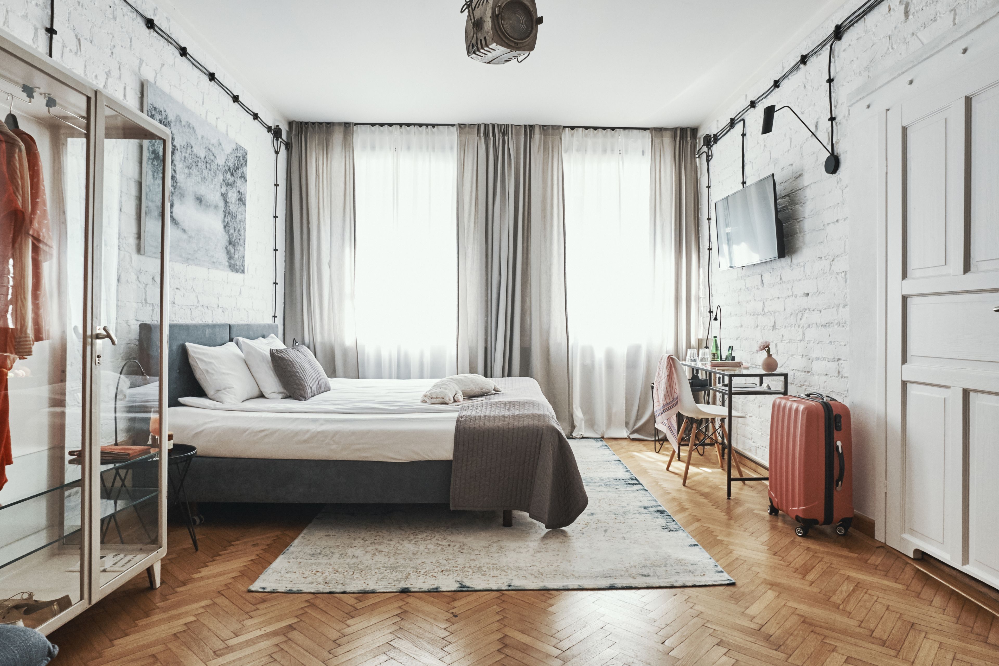 A modern bedroom with a bed, a wardrobe, a desk, a chair, and a suitcase.