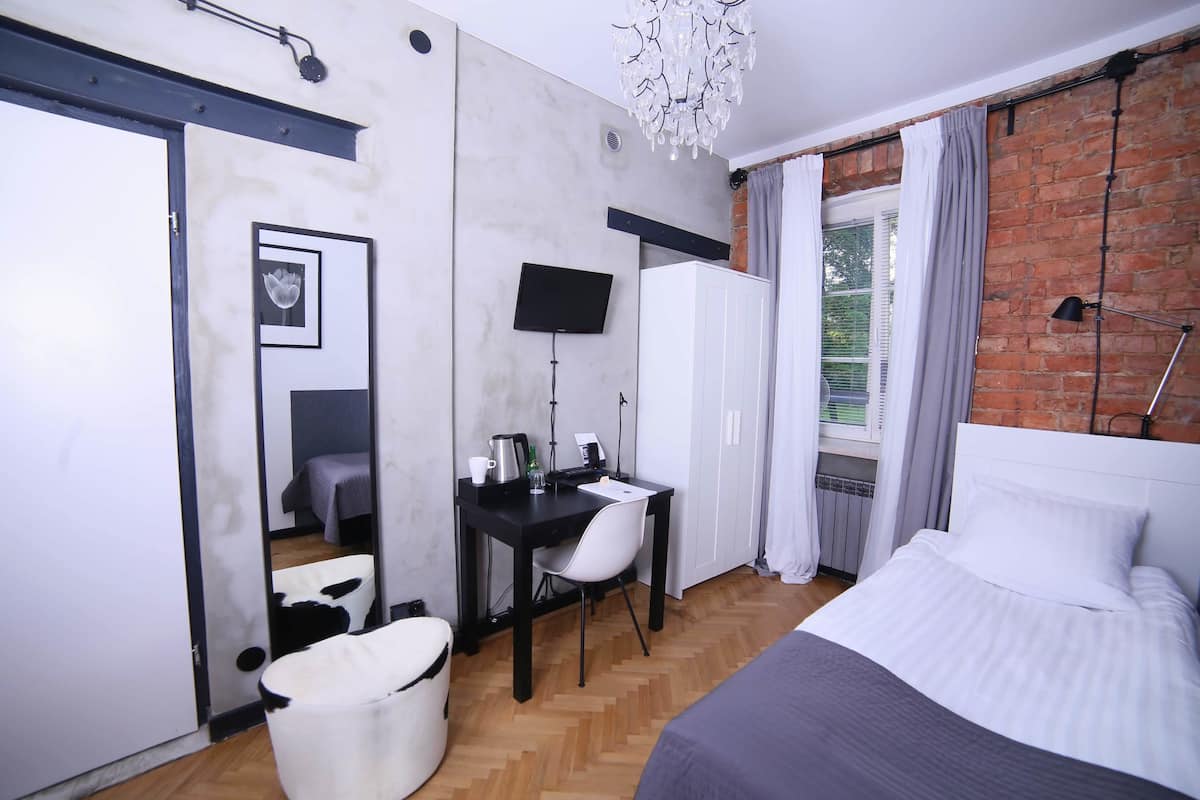 A modern bedroom with a bed, a desk, a chair, a TV, and a window with curtains.