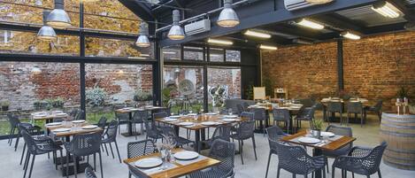 A restaurant with multiple tables and chairs, a brick wall, and hanging lights.