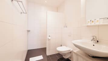 Un baño moderno con inodoro blanco, lavamanos y zona de ducha.