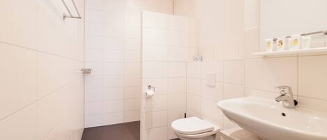 Un baño moderno con inodoro blanco, lavamanos y zona de ducha.