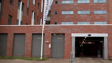 Un edificio de ladrillo rojo con un cartel blanco que dice "AMSTERDAM HOTEL". Hay tres grandes puertas de garaje y un letrero sobre la entrada.