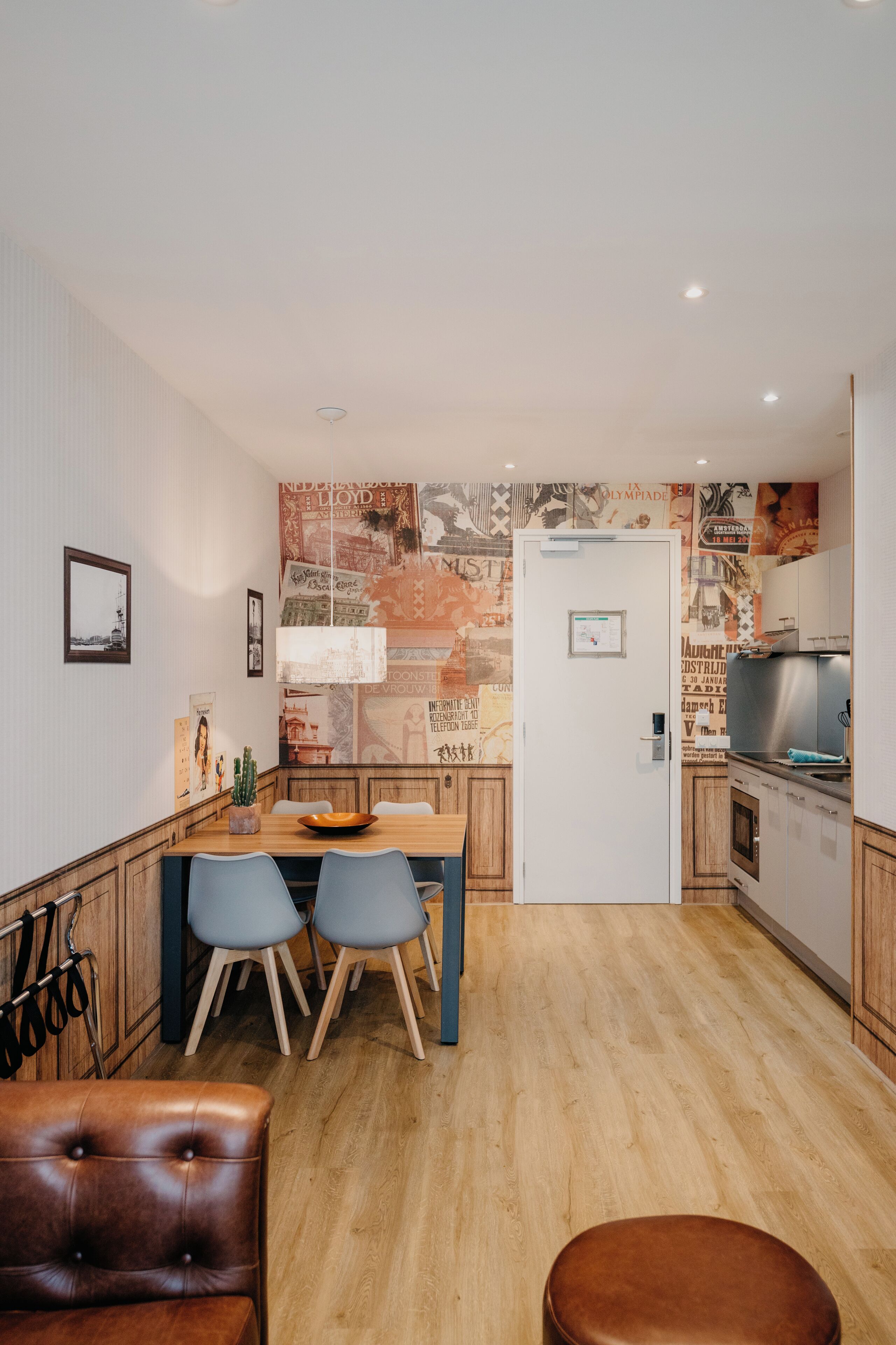 A compact kitchen with a dining area, wooden cabinets, a stainless steel refrigerator, and a wall with vintage posters.