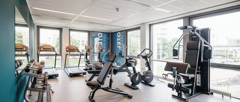 Une salle de sport équipée de machines de cardio, de bancs de musculation et de poids libres.
