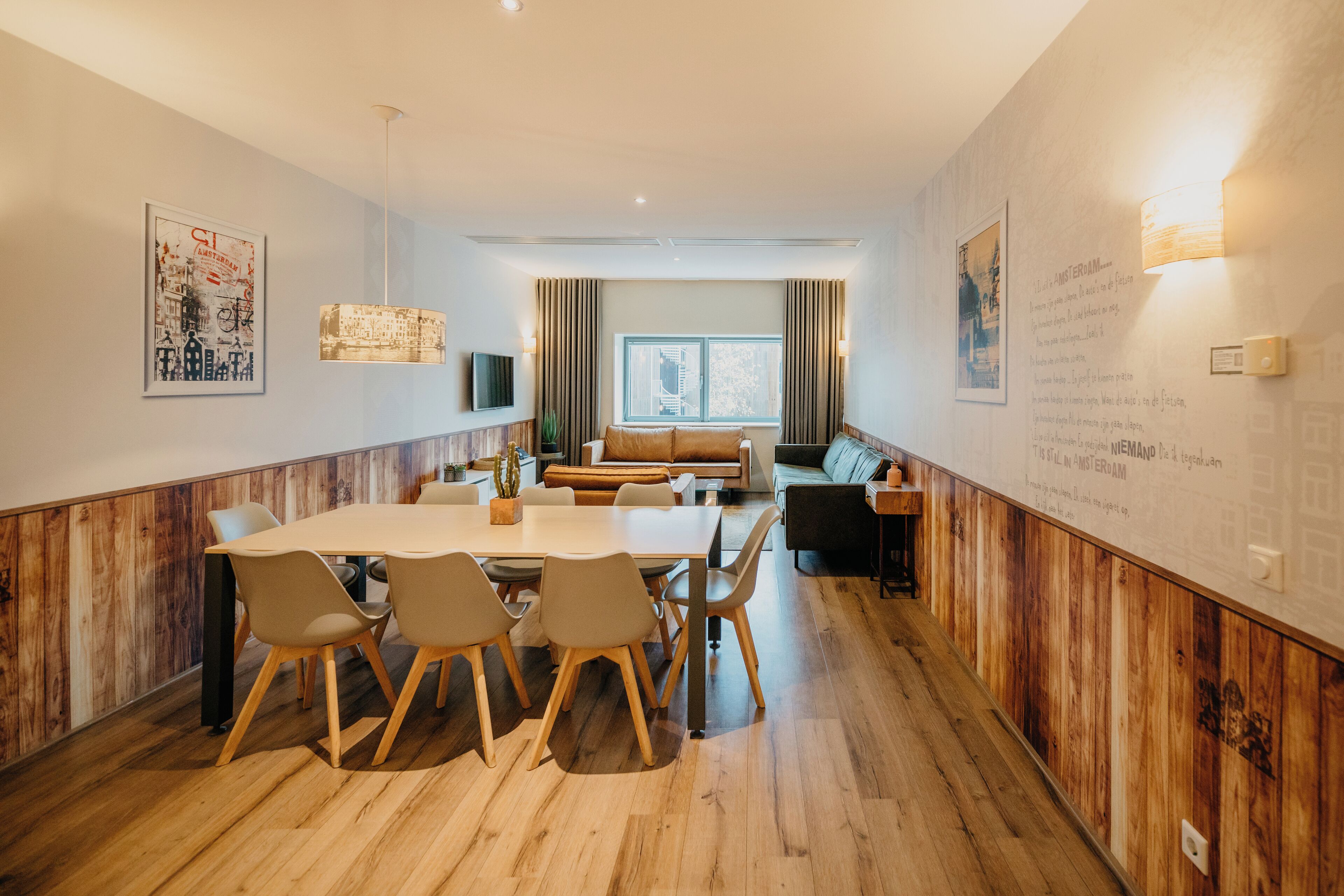 Un espace de repas moderne avec une table et des chaises en bois, un canapé et une grande fenêtre agrémentée de rideaux.