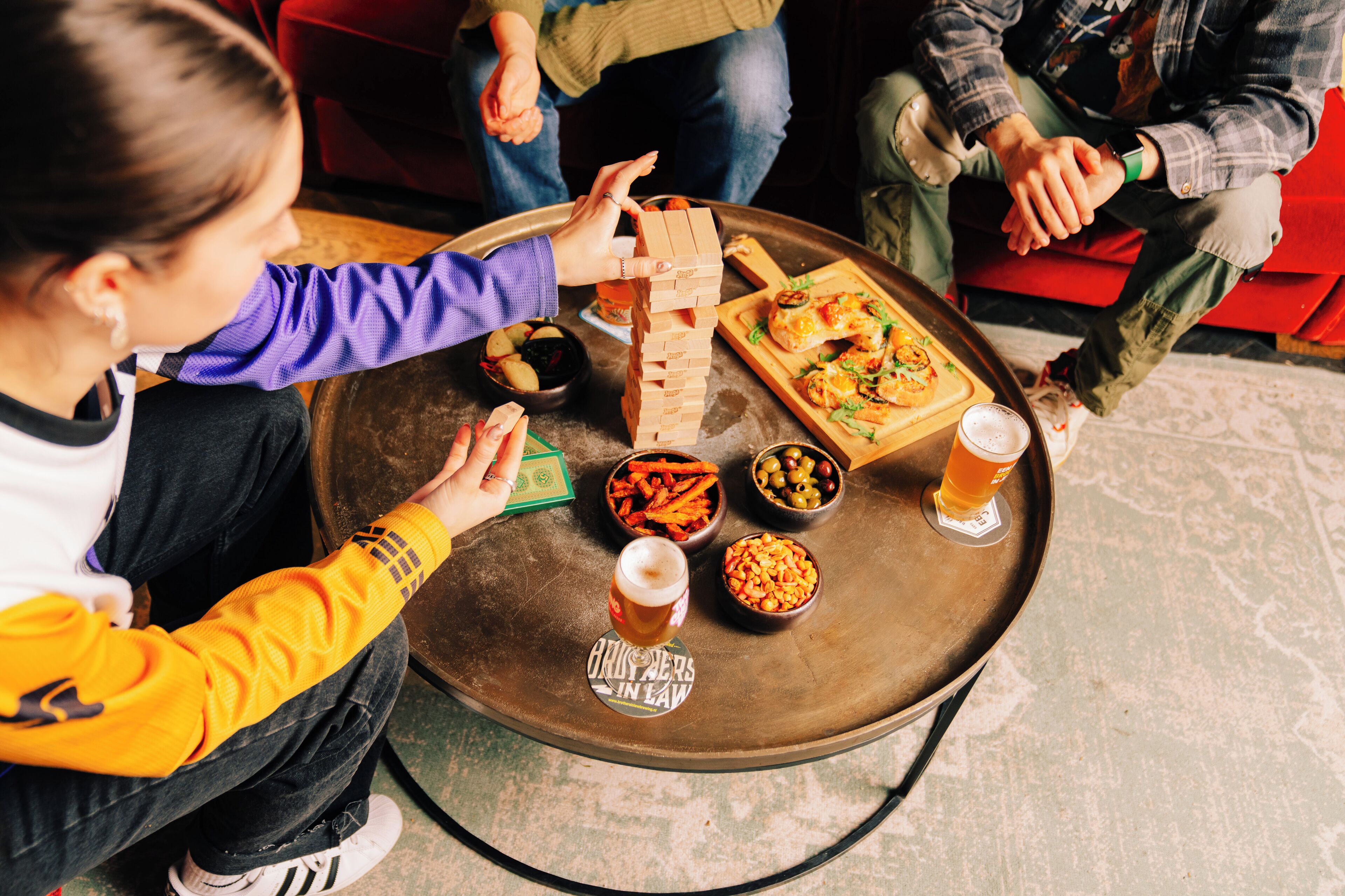 A group of people playing Jenga around a table with food and drinks.
