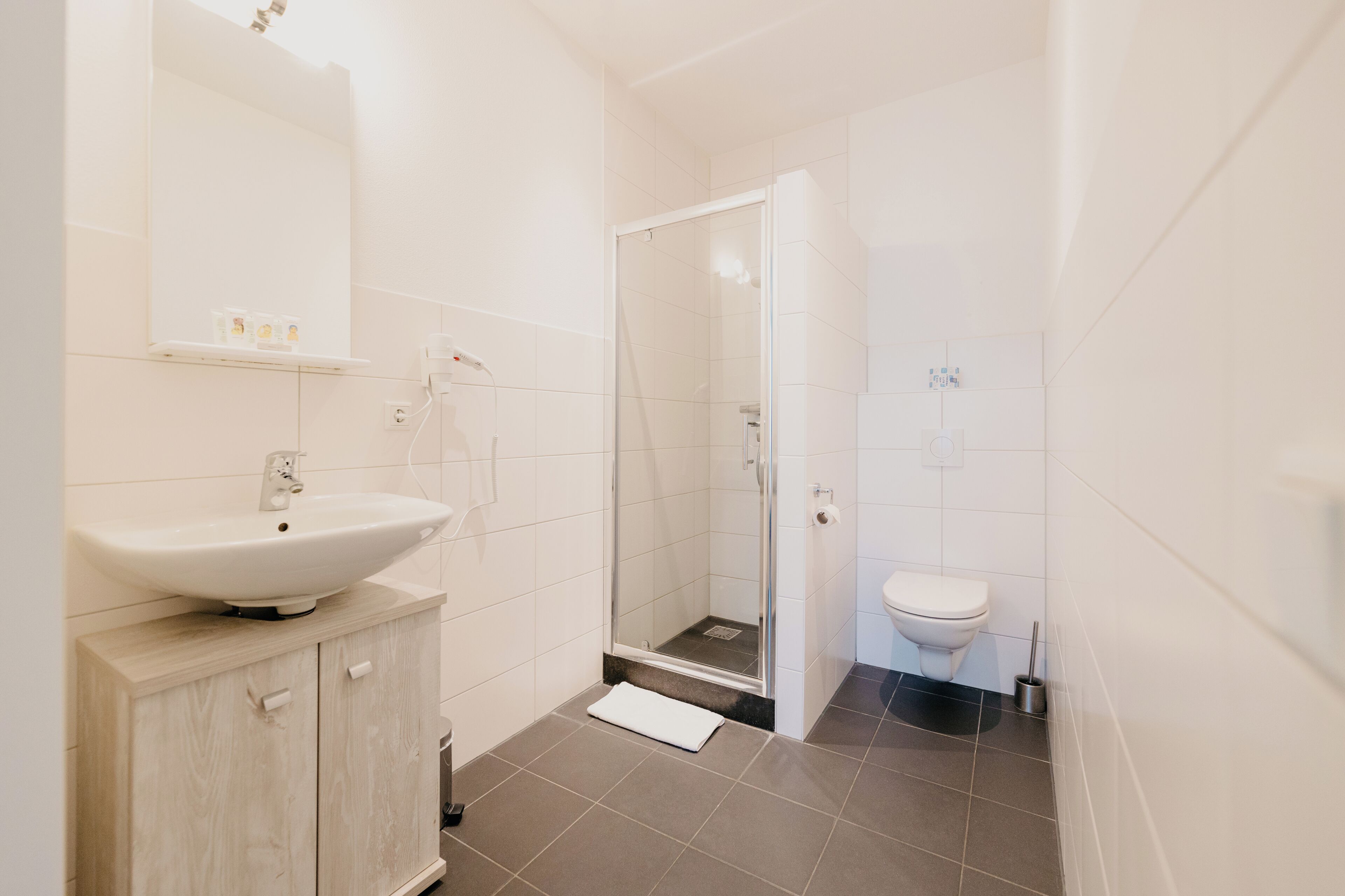 A modern bathroom with a sink, mirror, shower, and toilet.