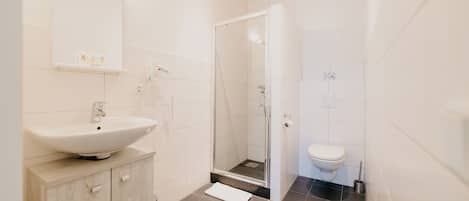 A modern bathroom with a sink, mirror, shower, and toilet.