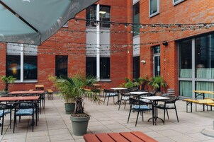 An outdoor patio area with brick walls, tables, chairs, and potted plants.