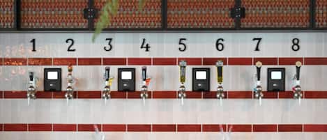 Una zona de bar con grifos numerados, una pared de azulejos y sillas verdes.