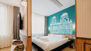 Habitación de hotel con cama, mesita de noche con lámpara, pared con un mural de paisaje urbano y ventana con cortinas.