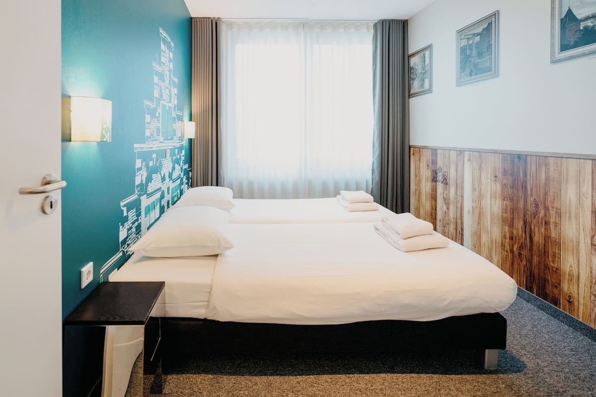 Une chambre d’hôtel avec un grand lit, une table de chevet, une lampe fixée au mur et une fenêtre avec des rideaux.
