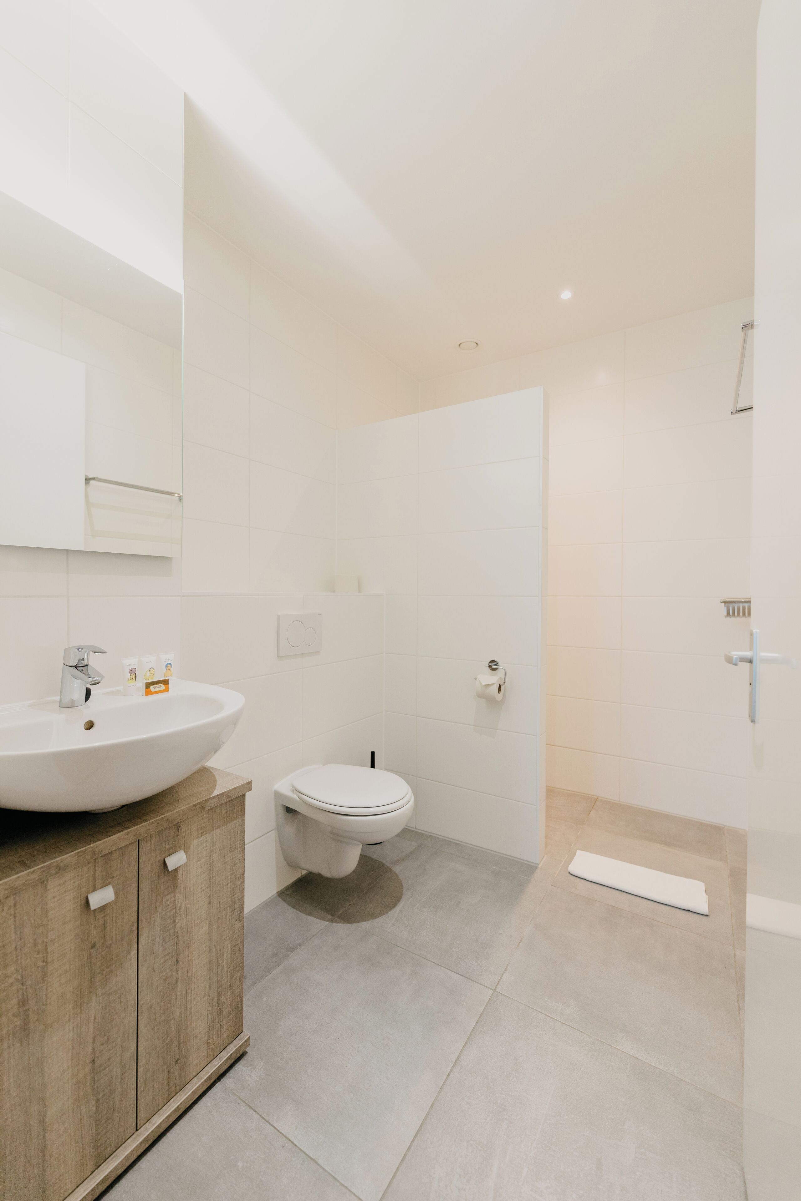 A modern bathroom with a wooden vanity, a white sink, a toilet, and a shower area.