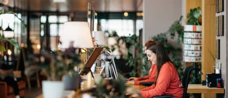 A person working at a desk in a well-lit indoor space with plants and shelves in the background.