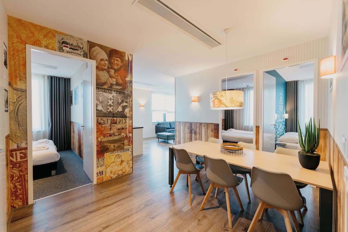 Une chambre d’hôtel moderne avec un plancher en bois, un coin repas comprenant une table et des chaises, un grand miroir et une plante en pot.