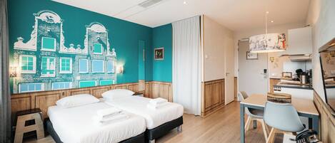 A hotel room with two beds, a desk, and a kitchenette.