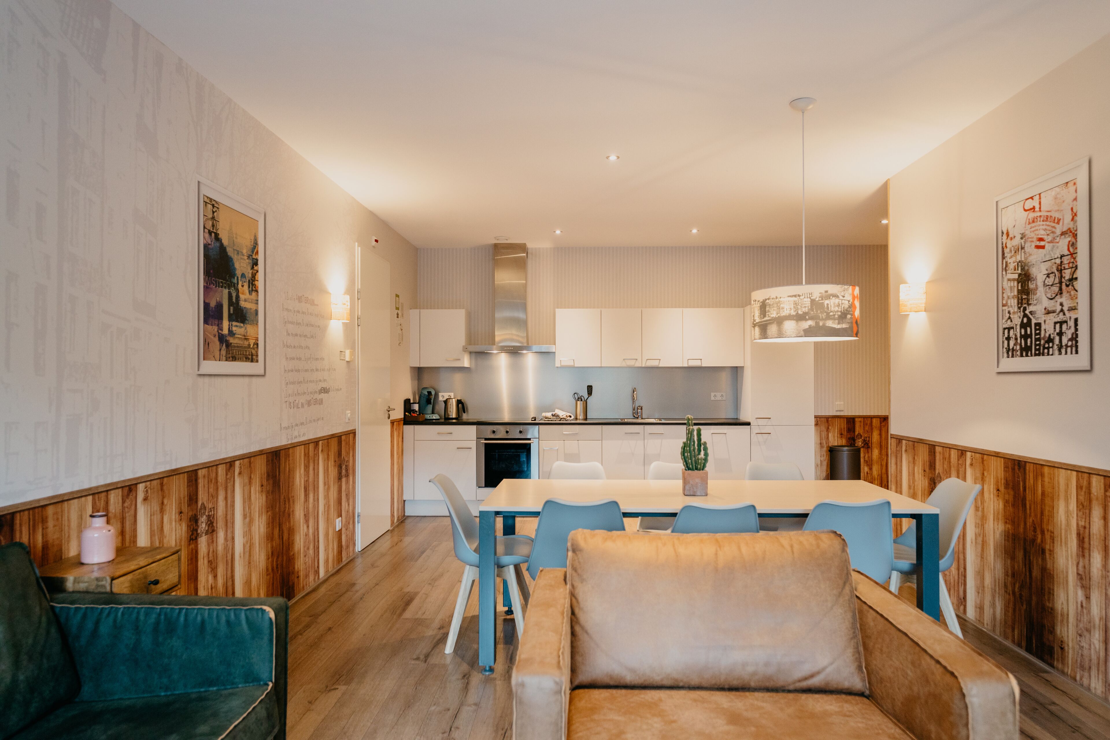 Une cuisine moderne avec des armoires blanches, une hotte en acier inoxydable et un coin repas comprenant une table en bois et des chaises bleues.