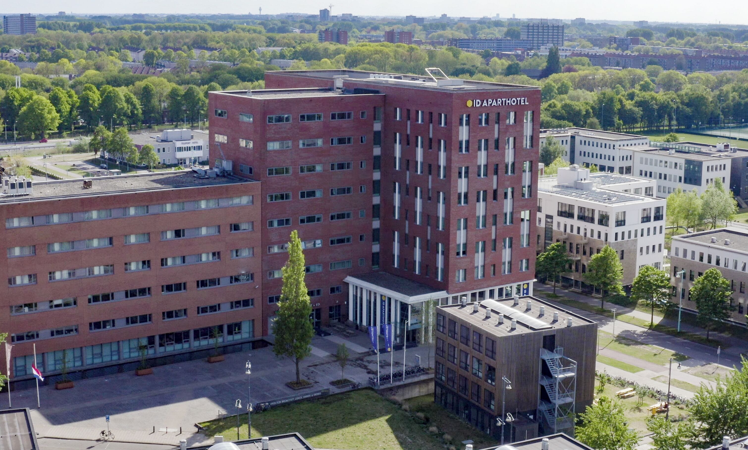 A multi-story hotel with a red brick facade, multiple windows, and a sign reading "ID APARTHOTEL".