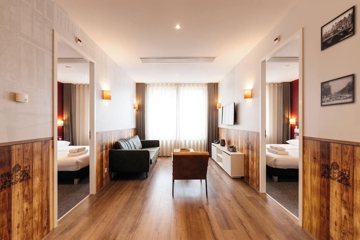 Une chambre d’hôtel avec un plancher en bois, un canapé, une petite table, un lit et un miroir.