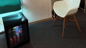 A room with a flat-screen TV displaying YouTube, a white chair, a wooden desk, a potted plant, and a beverage cooler with drinks. - Hotel Schwarzer Bär (Hannover)