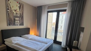 A hotel room with a large bed, a desk, a chair, a window with curtains, and a painting on the wall. - Hotel Schwarzer Bär (Hannover)