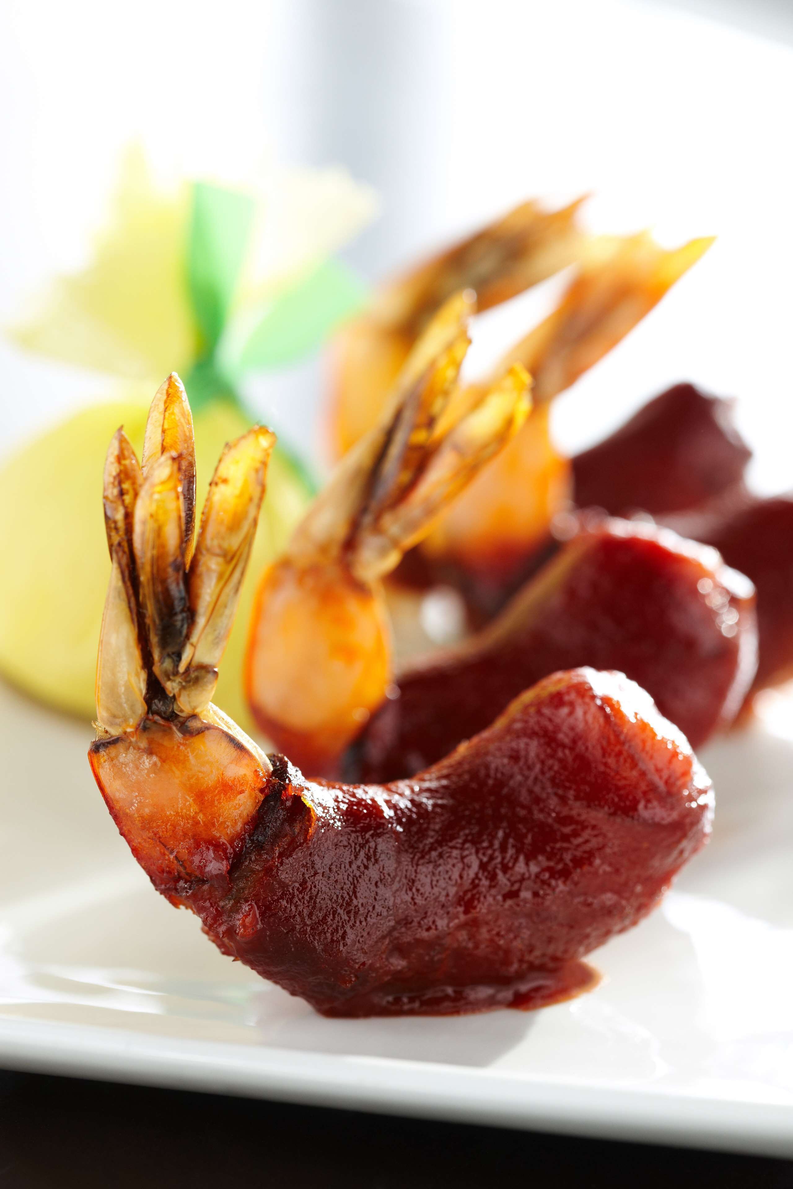 A plate with grilled shrimp and a slice of meat, possibly bacon, with a lemon wedge on the side.