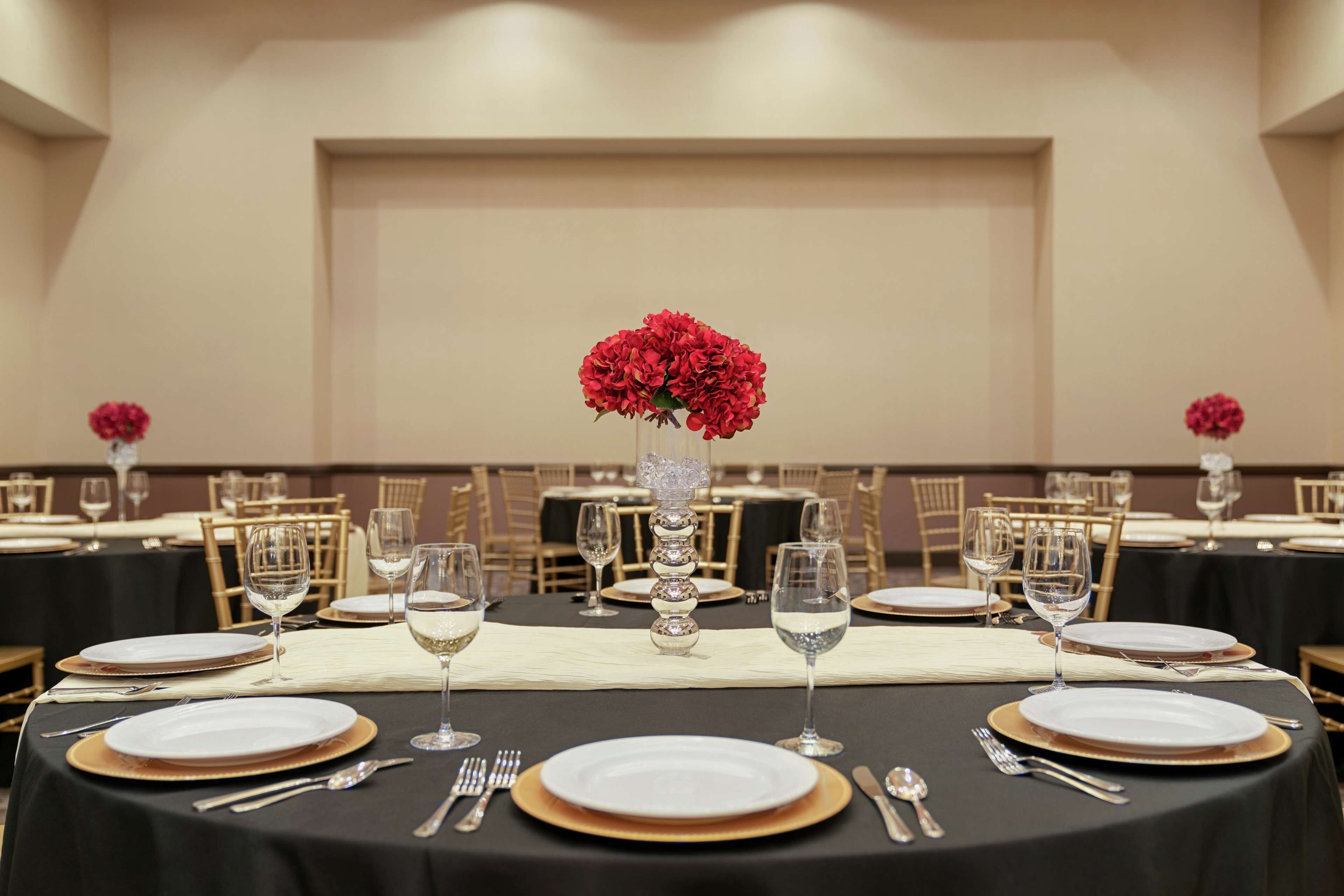 A banquet hall with tables set for a formal event, featuring white plates, gold chargers, and clear wine glasses.