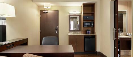Habitación de hotel con una mesa de comedor de madera, dos sillas, un televisor, un microondas, un lavabo y un armario.