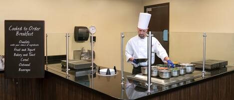 A breakfast buffet area with a chef preparing food.