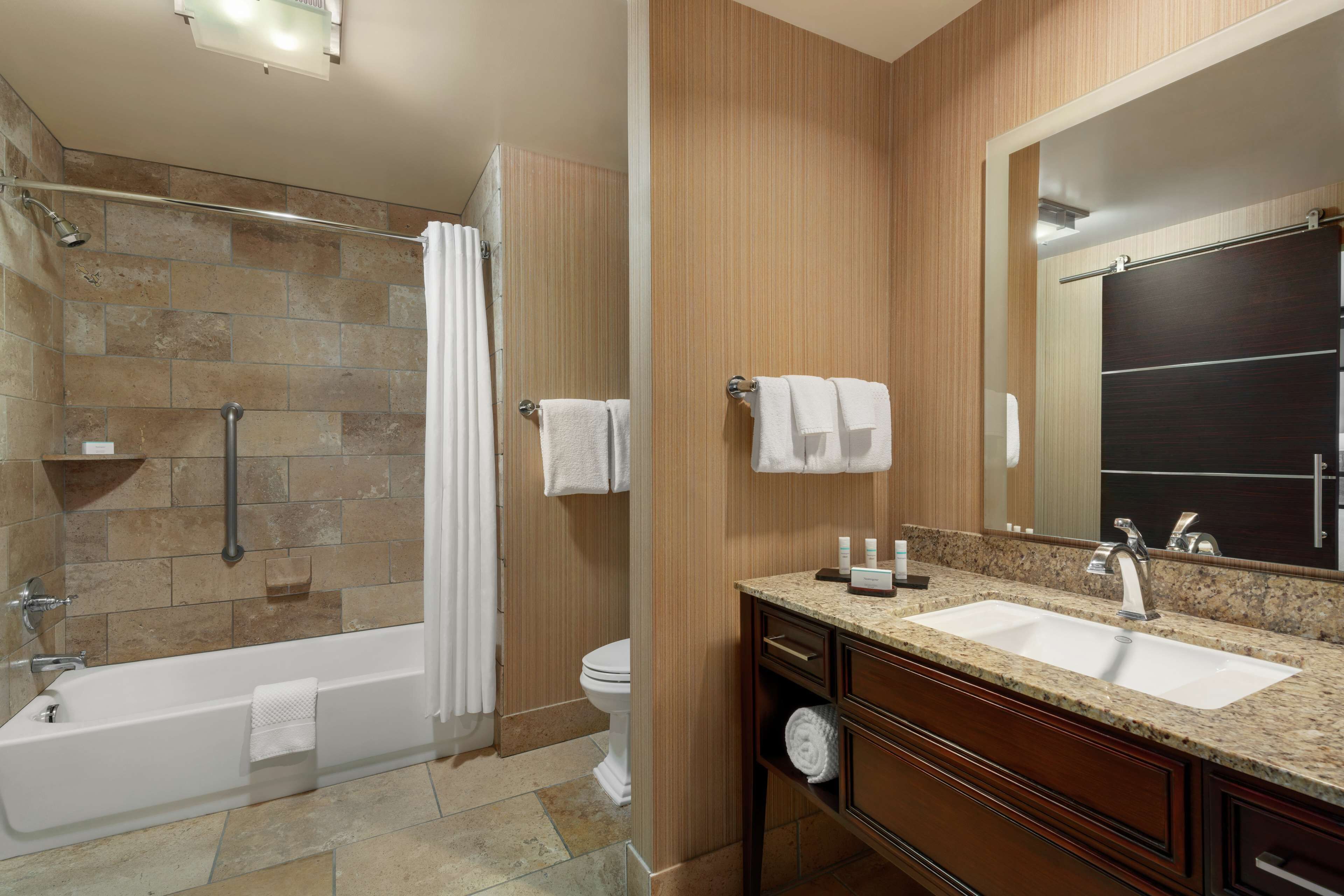 A modern bathroom with a bathtub, shower, toilet, and a vanity with a sink and mirror.
