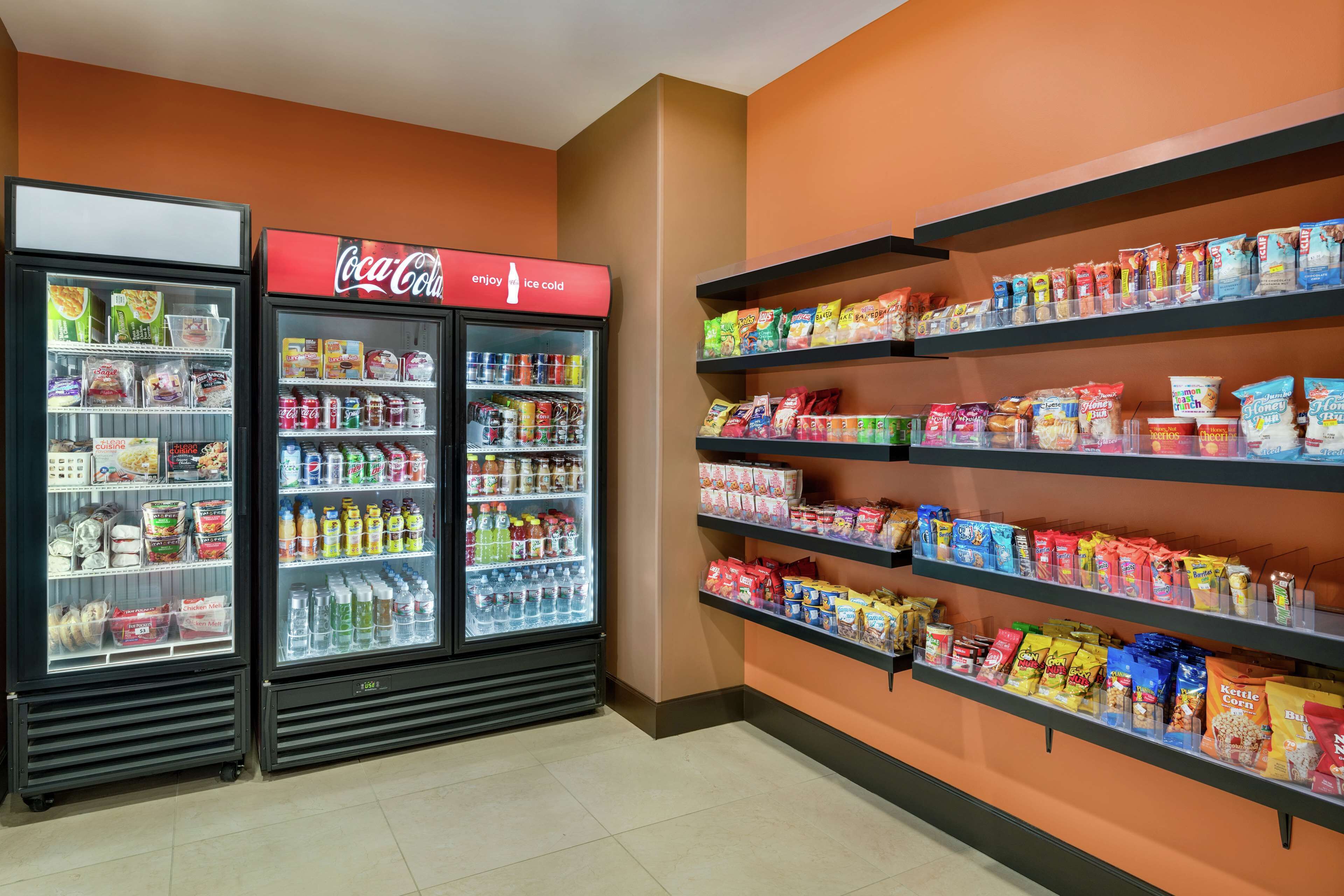 A snack and beverage display area with shelves stocked with various snacks and a Coca-Cola refrigerator.