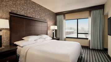 Habitación de hotel con una cama grande, una mesita de noche con lámpara, una ventana con cortinas y vistas al exterior.