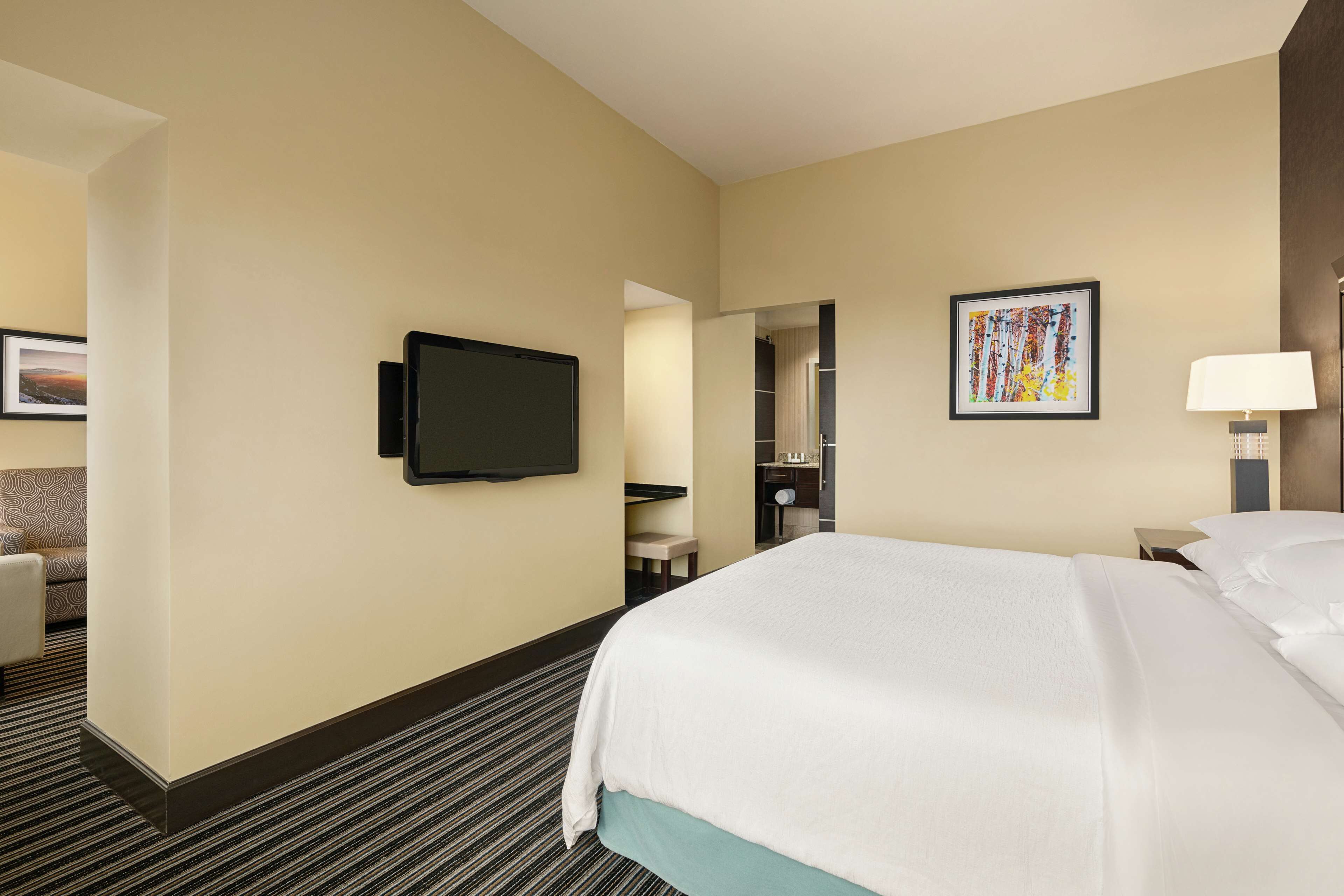 Een hotelkamer met een groot bed, een flatscreen televisie aan de muur, een nachtkastje met een lamp en een lijst met kunstwerk aan de wand.
