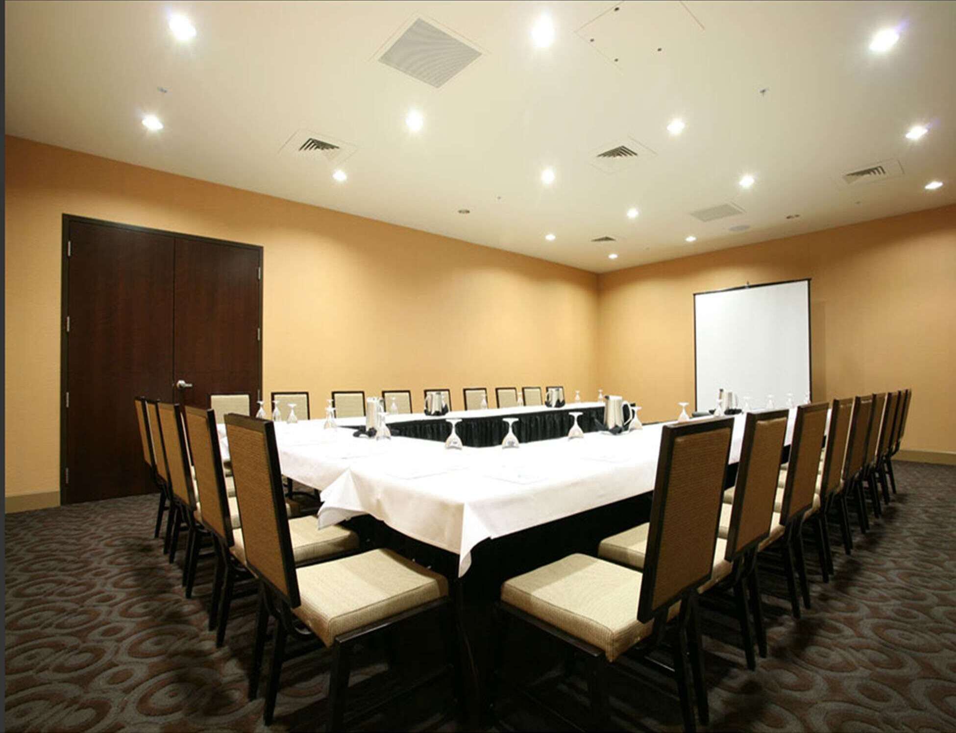 Un salón de conferencias con una larga mesa, sillas, una pantalla de proyector y una puerta.