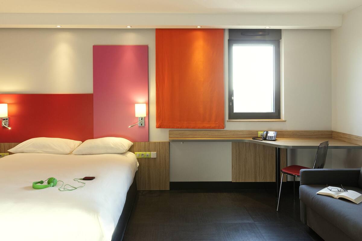 Une chambre d’hôtel avec un lit, un bureau, une chaise et une fenêtre.