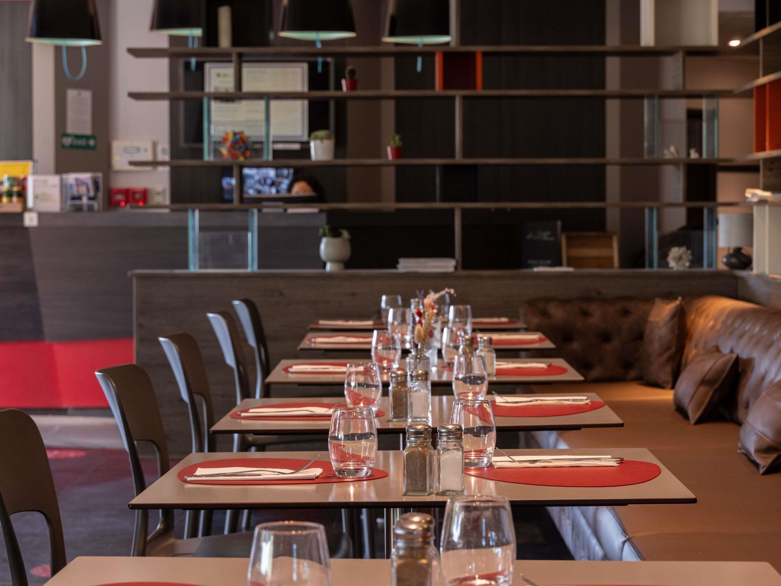 Een restaurant met gedekte tafels, een bankstel op de achtergrond en een plank met diverse spullen.